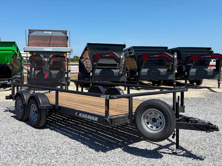 Black Karavan tandem-axle utility trailer with wood deck and mesh ramp gate, viewed from the opposite front three-quarter angle.